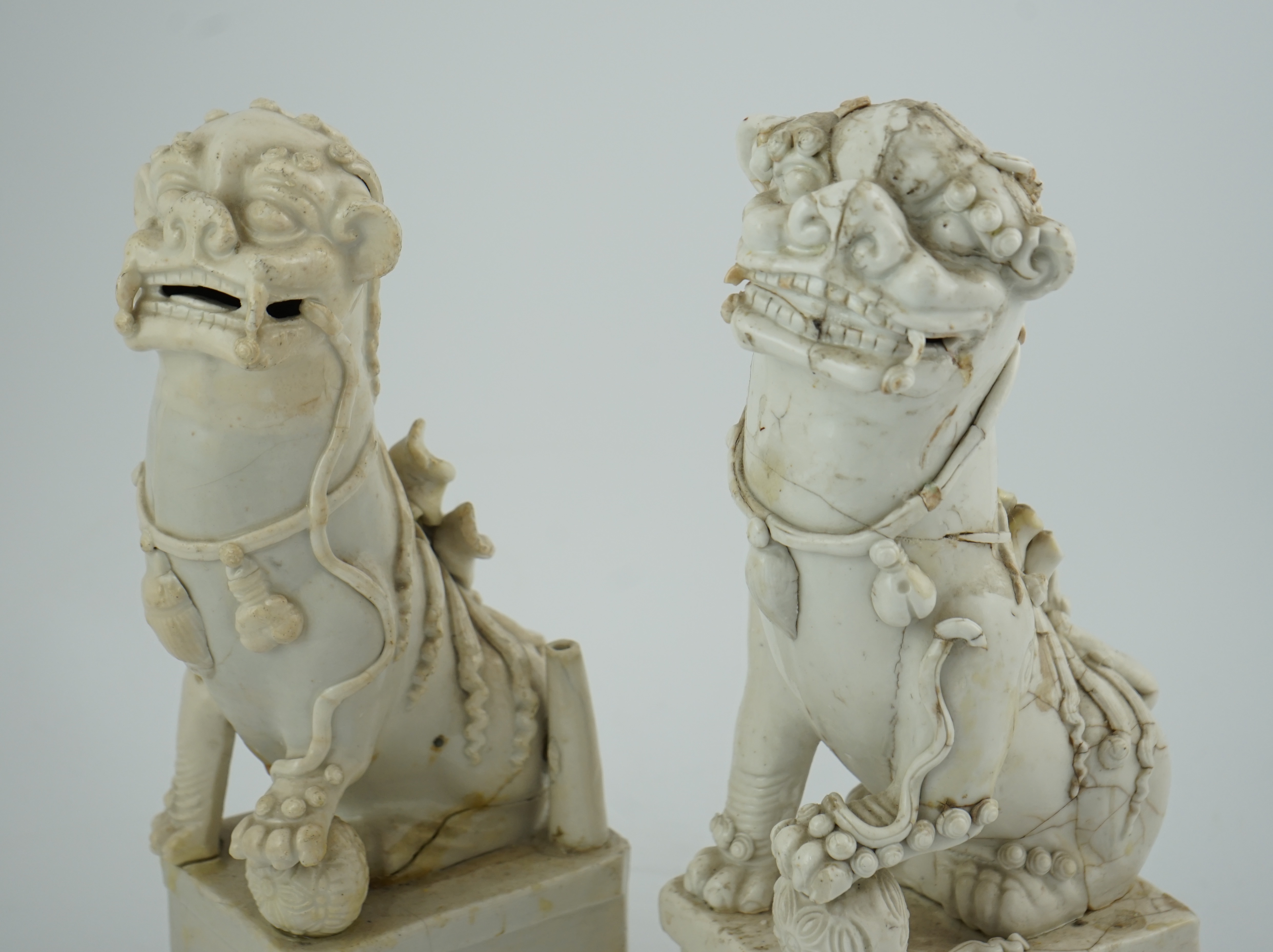 Two large Chinese Dehua blanc de chine Buddhist lion joss-stick holders, Kangxi period, each seated, one paw raised on a ball, on rectangular pedestal basis, 35cm high, Condition - extensive cracks or repairs